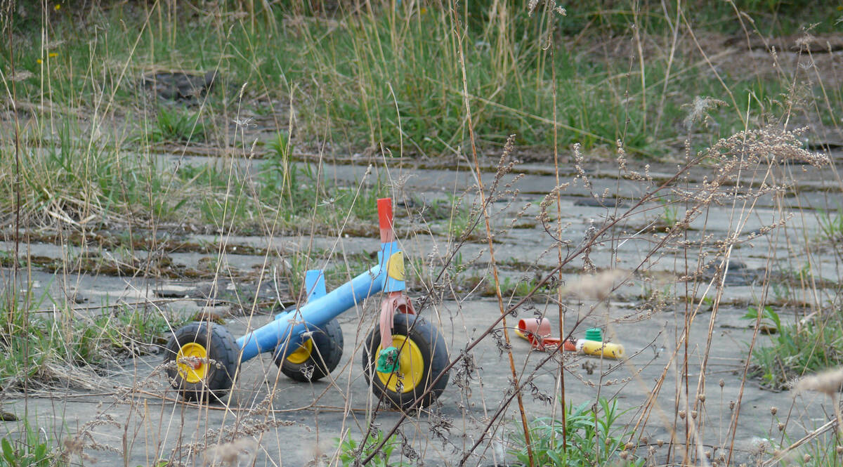 Dreirad mit zerbrochenem Lenker steht alleine auf grasdurchwachsenen Betonplatten.
