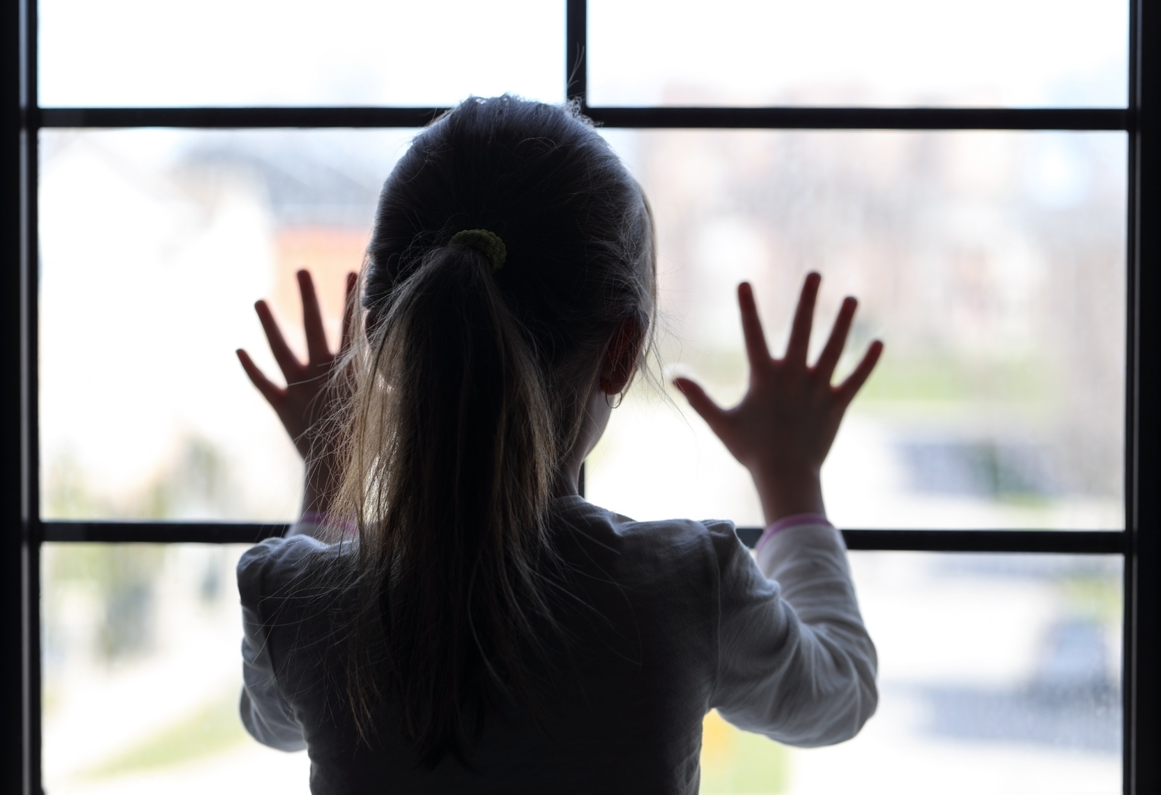 Kind im Schatten blickt aus dem hellen Fenster